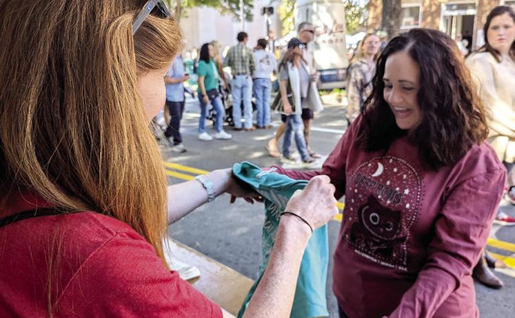Amber English (Left) shows Deep Roots merchandise to Amanda Webb. ANDREW BROWN/Staff