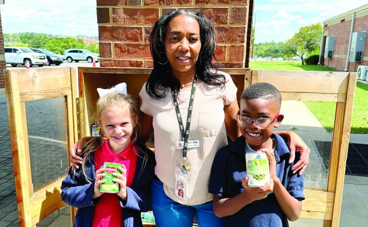 Midway Hills Primary STEAM teacher Katrina Veal poses with two students in front of the school’s food pantry to show off the canned goods students stocked the pantry with. CONTRIBUTED