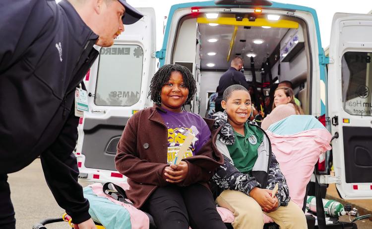A pair of Midway Hills Academy students sit on a stretcher as they wait for students inside Atrium Health Navicent’s ambulance to finish their tour.