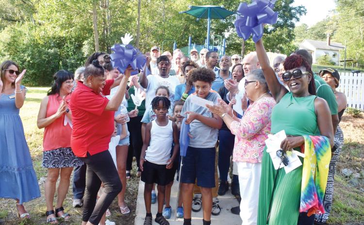 The Baldwin County Board of Commissioners, state officials, and members of the Milledgeville-Baldwin Chamber of Commerce cheer as local youth cut the ribbon to officially open Oconee Heights Mini Park. BAILEY BALLARD/Staff