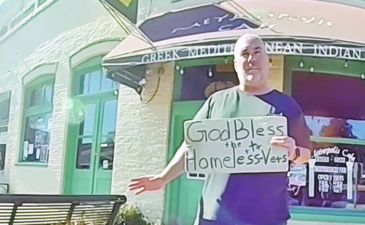 Jeffrey Gray stands with his “God Bless the Homeless Vets” sign while talking to police about why he will not move from the sidewalk unless trespassed. SCREENSHOT